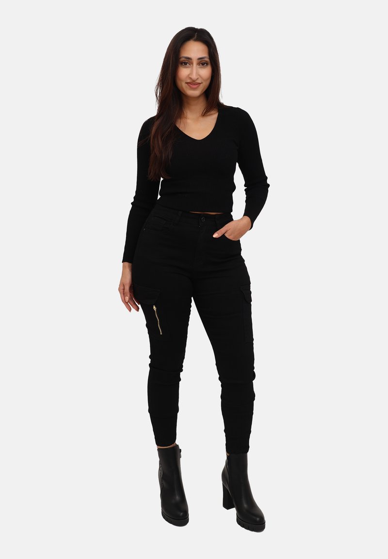 Schwarzes, geripptes Langarmoberteil mit V-Ausschnitt, kombiniert mit schwarzen Cargo-Hosen mit Reißverschlusstaschen und schwarzen Ankle-Boots. Minimalistisches Design.