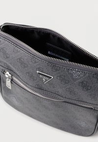 Šedá taška Guess s texturovaným povrchem, detaily loga a stříbrným zipem. Obsahuje jednu kapsu na zip a vnitřní podšívku.