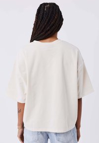T-shirt a maniche corte, di colore crema, morbido al tatto, con scollo rotondo e una sottile cucitura nel retro.