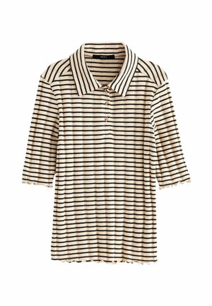 Femme portant un pantalon large beige et un haut rayé crème à manches courtes, tenant un sac à main en cuir marron sur un fond olive.