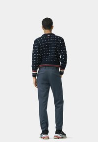 Marineblauer Strickpullover mit weißen Punkten, geripptem Bündchen, kombiniert mit schiefergrauen Hosen und schwarzen Sneakers mit bunten Akzenten.