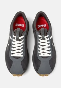 Scarpe da ginnastica grigie con lacci bianchi e soletta rossa. Le caratteristiche includono una tomaia texturizzata con pannelli a contrasto e una suola in gomma.