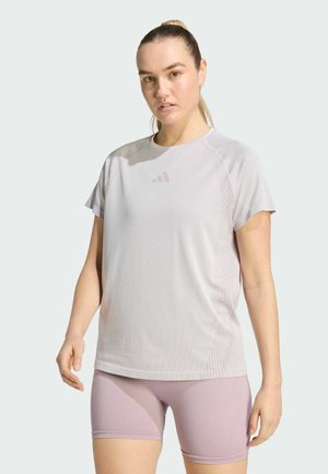 Maglietta sportiva grigio chiaro con maniche corte, texture a coste e logo discreto. Abbinata a pantaloncini aderenti di colore viola chiaro.