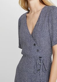 Marineblaues Kleid mit weißen Polka-Dots, V-Ausschnitt, kurzen Ärmeln, Knopfdetails auf der Vorderseite und einem Taillengürtel zur Anpassung der Passform.