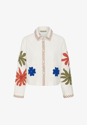 Veste blanche boutonnée avec bordure en zigzag rouge et verte, ornée de grandes appliques de fleurs rouges, vertes et bleues sur les manches et les poches avant.