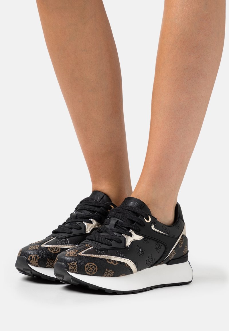 Schwarze Sneakers mit goldenen Akzenten, ausgestattet mit einem strukturierten Leder-Obermaterial, gemusterten Details und einer weißen Gummisohle. Schnürdesign für einen sicheren Sitz.