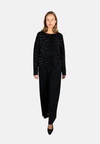 Schwarzer, strukturierter Pullover mit einem Leopardenmuster, kombiniert mit lockeren, schwarzen Rippenhosen und schwarzen spitzen Schuhen.