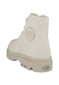Botte de cheville en toile blanche avec semelle en caoutchouc, patch logo rond sur le talon et couture texturée. Présente un devant à lacets et un col haut.