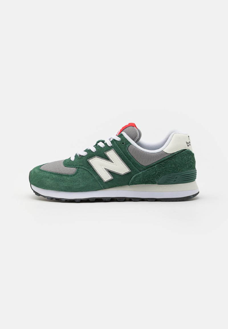 Zapatilla de ante verde y malla gris con acentos blancos, que presenta un destacado logo "N" y un detalle en rojo en el talón. Diseño clásico de suela de goma.
