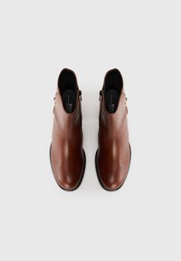 Brune skinnankelstøvler med en glatt finish, glidelås og en liten spennfiner på siden. Sleek, avrundet tådesign.