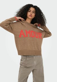 Brūns adīts džemperis ar spilgtu sarkanu "AMOUR" tekstu, īsa forma, plata dekoltē un ribotām malām. Saskaņots ar gaiši beidz uzvalku.
