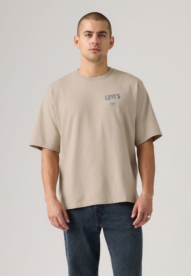 T-shirt bege Levi's 501, mangas curtas, gola redonda, tecido macio, logo frontal em cinza, combinada com jeans denim escuro.