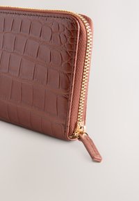 Brown crocodile-embossed leather wallet with a gold zipper, featuring a textured surface and a small zipper pull tab.