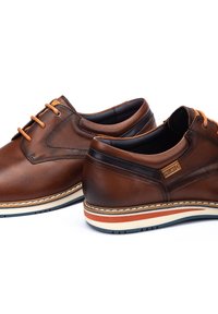 Brown leather shoes with a smooth texture, featuring a lace-up design, contrasting orange laces, and a striped rubber outsole.