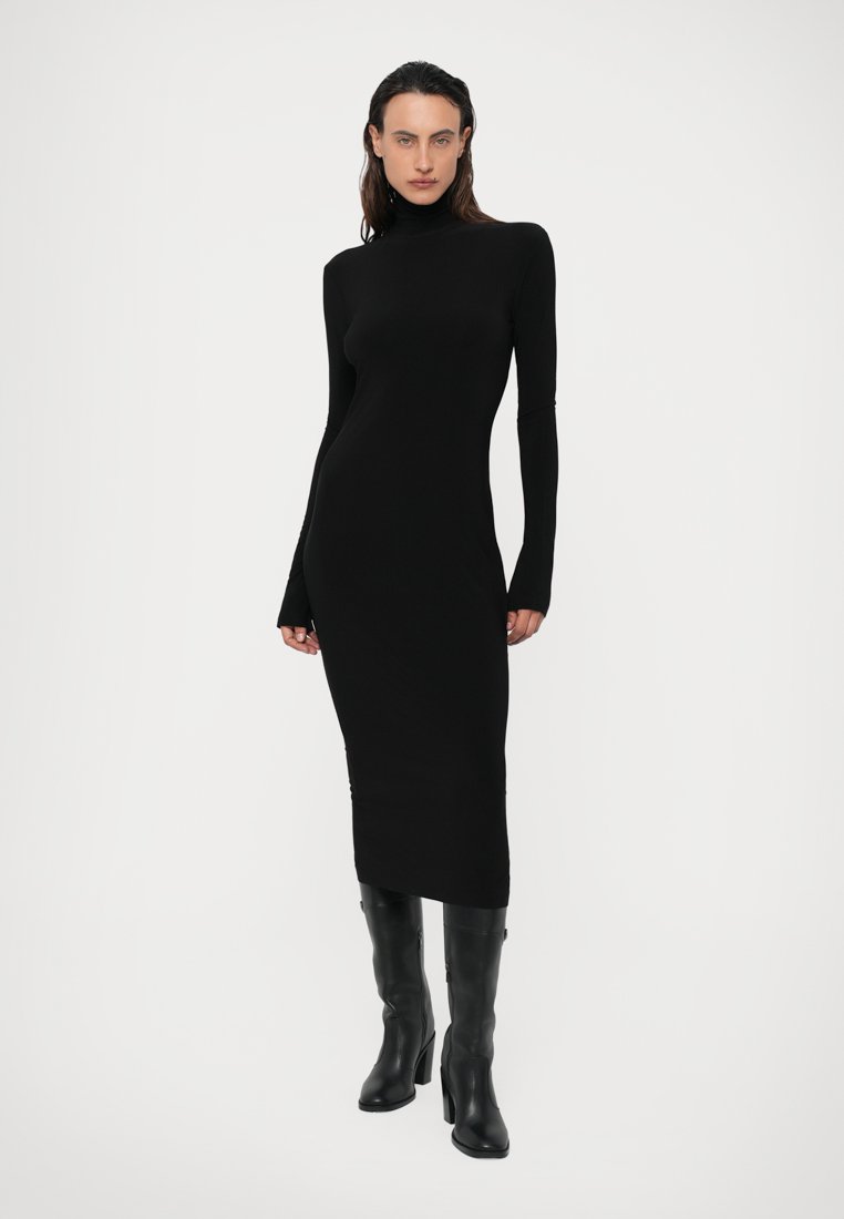 Robe moulante noire à col montant, en matériau lisse et extensible, avec des manches longues et une longueur midi, assortie de bottes noires jusqu'aux genoux.