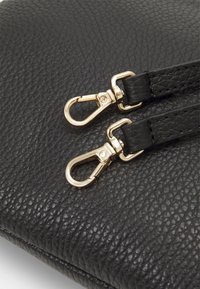 Sac en cuir noir avec une surface texturée, deux clips en métal doré et des poignées noires lisses.