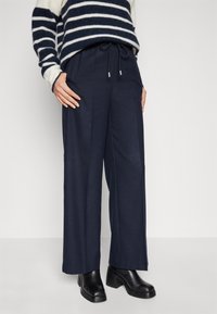 Marina vida byxor med elastisk dragsnöre i midjan, mjukt tygn, och slät frontfinish, i kombination med svarta klackstövlar.