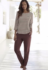 Camiseta de manga larga a rayas en marrón y crema combinada con pantalones burdeos, ambos de tejido suave, con un corte holgado y un diseño sencillo.