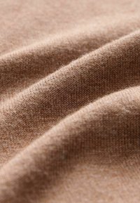 Tissu tricoté beige avec une surface douce et texturée, présentant de subtiles variations de couleur ainsi qu'une série de doux plis et froissements.