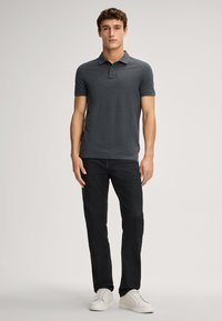 Dunkelgraues Polohemd mit kurzen Ärmeln, Knopfleiste mit drei Knöpfen und Logodetail, kombiniert mit dunkelblauen Jeans und weißen Turnschuhen. Glatte Textur.