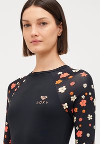 Mustakirjaga ujumistopp pika varrukaga, kaunistatud punaste, oranžide ja valgete lillemusterdega. Esiosas on väike kuldne "ROXY" logo.