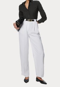 Camisa negra de botones, pantalones blancos de cintura alta con pliegues, cinturón negro con hebilla dorada y bailarinas negras con punta. Los acentos incluyen un bolso negro.