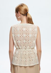 Top in crochet color beige con un design floreale testurizzato, vita arricciata, senza maniche e scollatura rotonda.