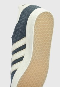 Blå textil-sneaker med vit gummisula, som har tre horisontella ränder, texturerat mönster på ovandelen och hexagonalt mönster på sulan.