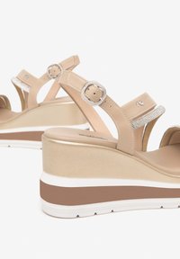 Sandales compensées beige avec des sangles en cuir texturé et des accents de boucle en argent. Détails scintillants remarquables sur la sangle et couleurs de semelle contrastantes.