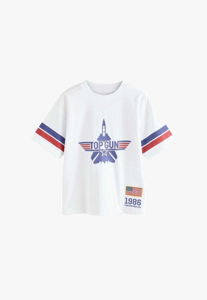 T-shirt bianca a maniche corte con strisce blu e rosse sulle maniche, logo "TOP GUN" con grafica di jet e toppa con bandiera USA e testo "1986".