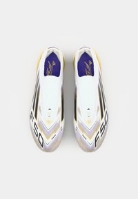 Baskets de football blanches au design épuré, avec des accents violets et dorés, des rayures noires et des motifs de surface texturée pour la traction.