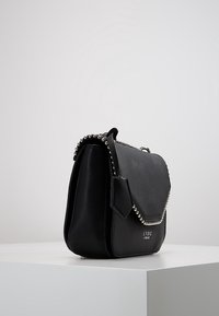 Borsa a tracolla nera in ecopelle, con una forma strutturata, adornata con accenti di borchie argentate lungo il flap e la tracolla. Include un'etichetta rimovibile.