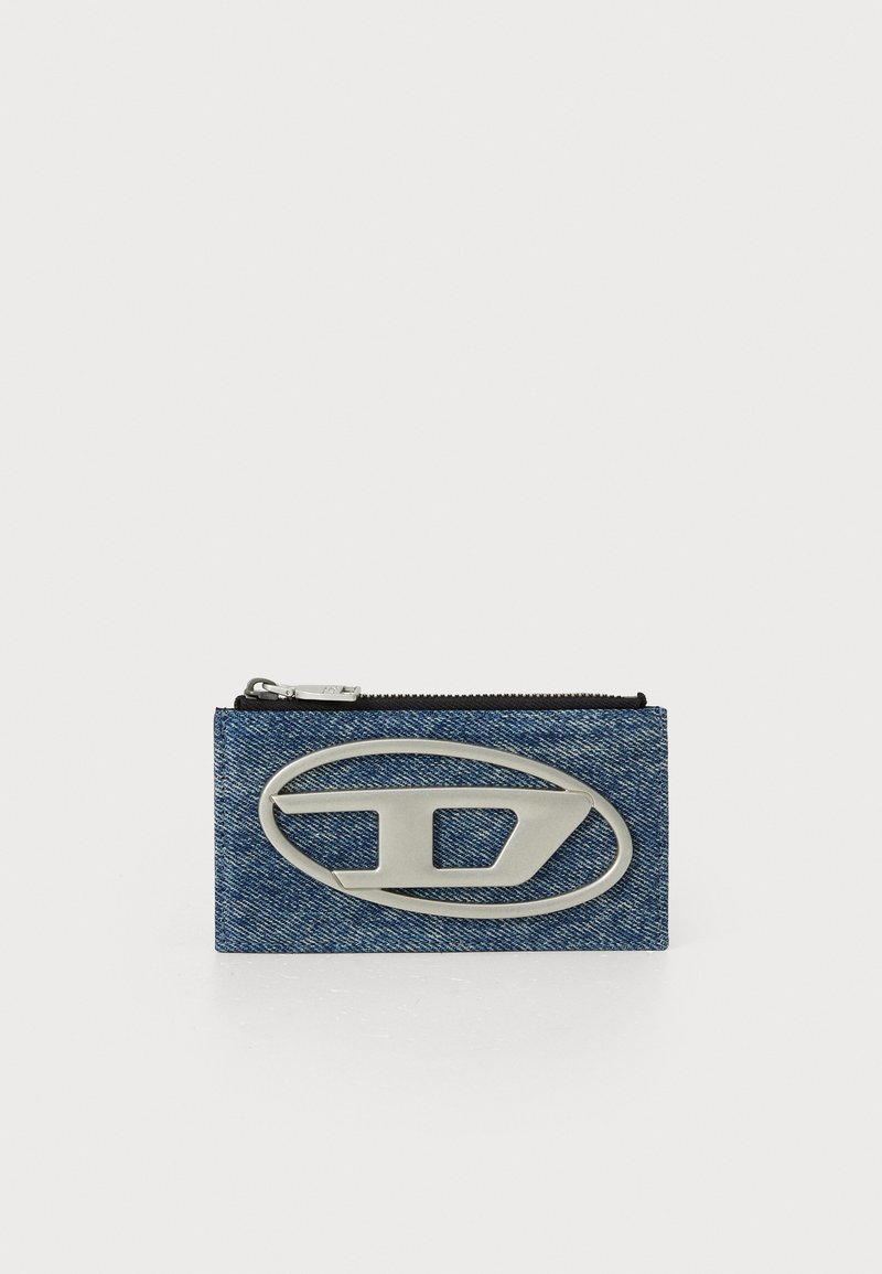 Denim zippered wallet featuring a large silver logo on the front. The material has a textured look consistent with denim fabric.