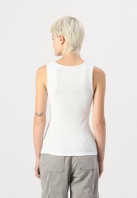 Débardeur blanc à côtes avec un col rond et une coupe slim, fabriqué en tissu léger. Ne présente aucun élément de quincaillerie ou motif visible.