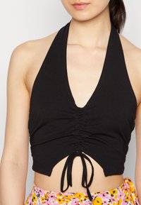 Top cropped preto com decote em V profundo, textura franzida na parte da frente e um detalhe atado na barra. Tecido suave com silhueta ajustada.