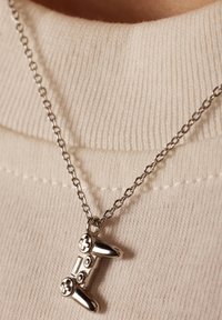 Zilverkleurige ketting met een hanger in de vorm van een gamecontroller, met details op de knoppen en een verstelbare ketting.