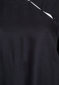 Black fabric top with a smooth texture, featuring a unique design with white underlayer visible at the shoulder and button accents.