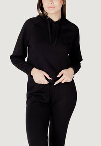Czarna bluza z kapturem i sznurkiem, z subtelnym detalem logo. Połączona z dopasowanymi czarnymi spodniami, obie z miękkiego, gładkiego materiału.