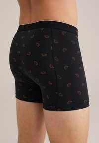 Juodos boxer tipo kelnaitės su pakartojančiu mažų raudonų ir žalių arbūzų griežinėlių raštu. Pagamintos iš tamprios medžiagos su elastinga juosmens juosta.