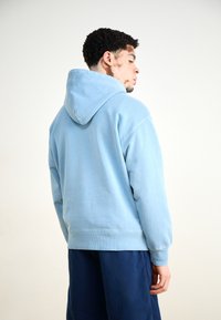 Light blue hooded sweatshirt with a relaxed fit, ribbed cuffs, and hem. Soft texture and unfinished hem details enhance casual design.