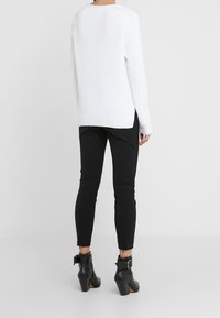 Biały dziany sweter o prążkowanej fakturze, z bocznymi rozcięciami, w zestawie z czarnymi wąskimi spodniami i czarnymi botkami z klamrami.