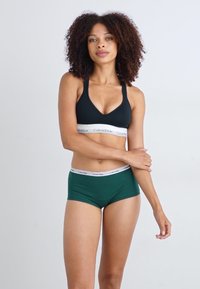 Black sports bra with a Calvin Klein logo band, paired with green boyshorts featuring a matching logo waistband. Simple, seamless design.