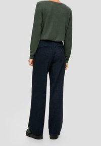 Maglietta verde a maniche lunghe abbinata a pantaloni navy a gamba larga con un delicato motivo a righe, completata da scarpe nere piatte.
