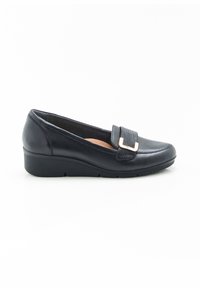 Zapato negro de piel tipo slip-on con un tacón bajo en cuña, que presenta una correa texturizada y un detalle metálico en la parte delantera. Acabado liso.