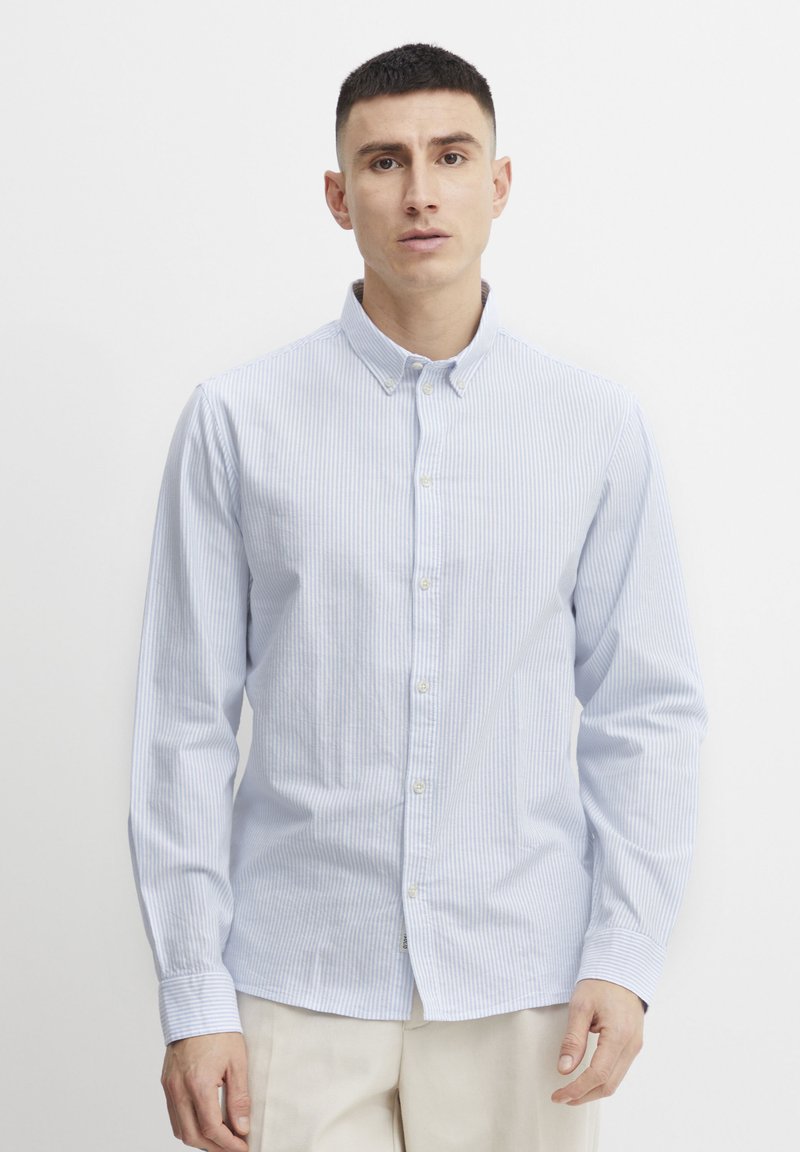 Camisa de botones a rayas azul claro y blanca, con mangas largas y cuello; presenta una textura suave y un diseño clásico.
