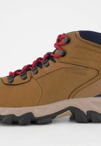 Beżowe buty trekkingowe z syntetycznej skóry, czerwonymi sznurówkami i gumową podeszwą. Posiadają czarne oczka i siateczkowe detale na kostce dla lepszej wentylacji.