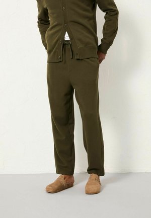 Olivgrüne Jogginghose und passender Cardigan aus weichem Material, mit Knopfleiste und Kordelzugbund, kombiniert mit beigen Clogs.
