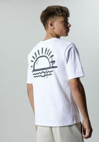 Camiseta de algodón blanca con un estampado gráfico negro de un sol sobre olas en la parte posterior. Cuello redondo, mangas cortas, corte relajado.