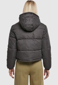 Mørk polstret, cropped jakke med hætte. Har quiltede sektioner og elastiske manchetter. Bæres med lyse, tætsiddende bukser.