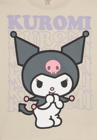 T-shirt w jasnobeżowym kolorze z centralnym nadrukiem kreskówkowej postaci w czerni i bieli z różowym czaszką, otoczonej fioletowym napisem "KUROMI".